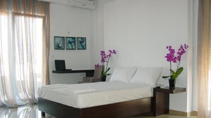 A modern bedroom with a large bed, a desk, and two potted orchids. - Harisis Apartments (Katerini)