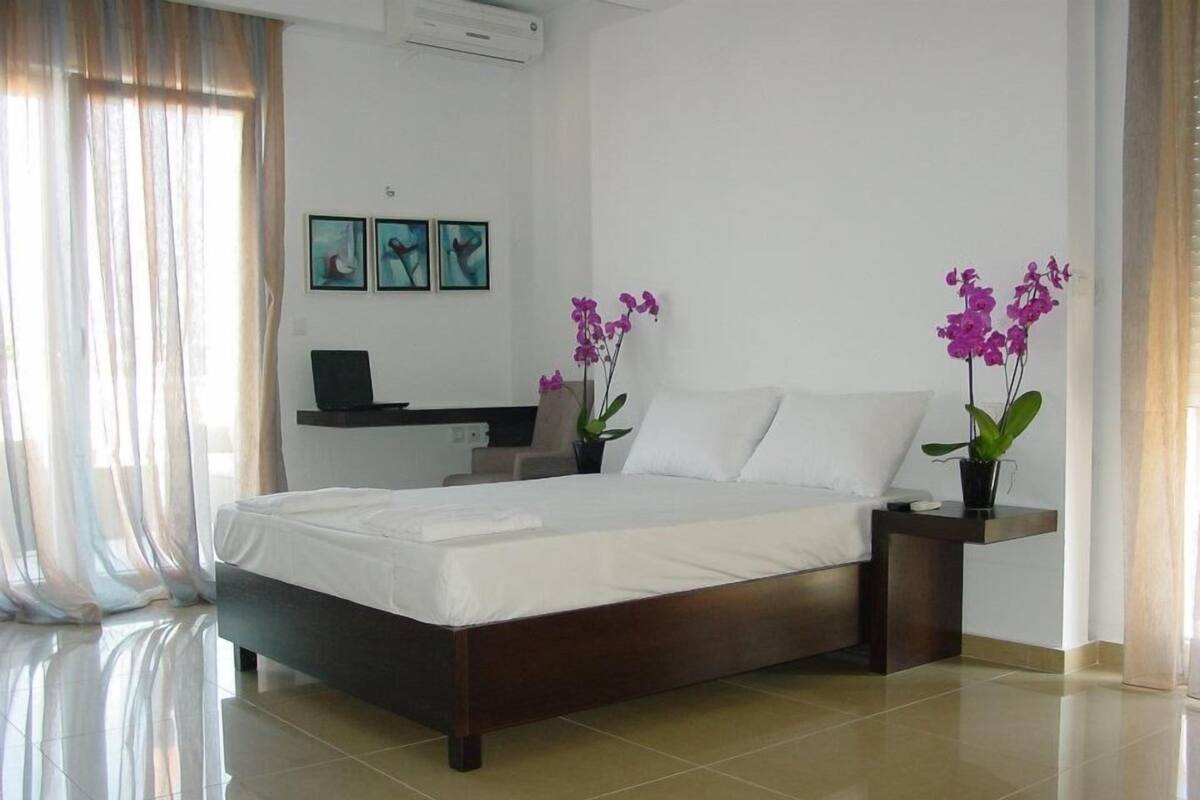 A modern bedroom with a large bed, a desk, and two potted orchids.