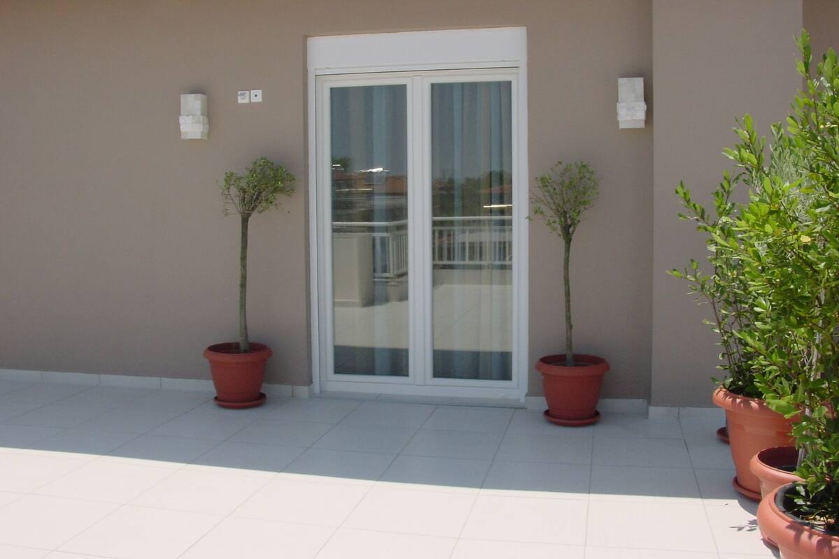 A building with a beige exterior, a white-framed glass door, and potted plants on the ground.