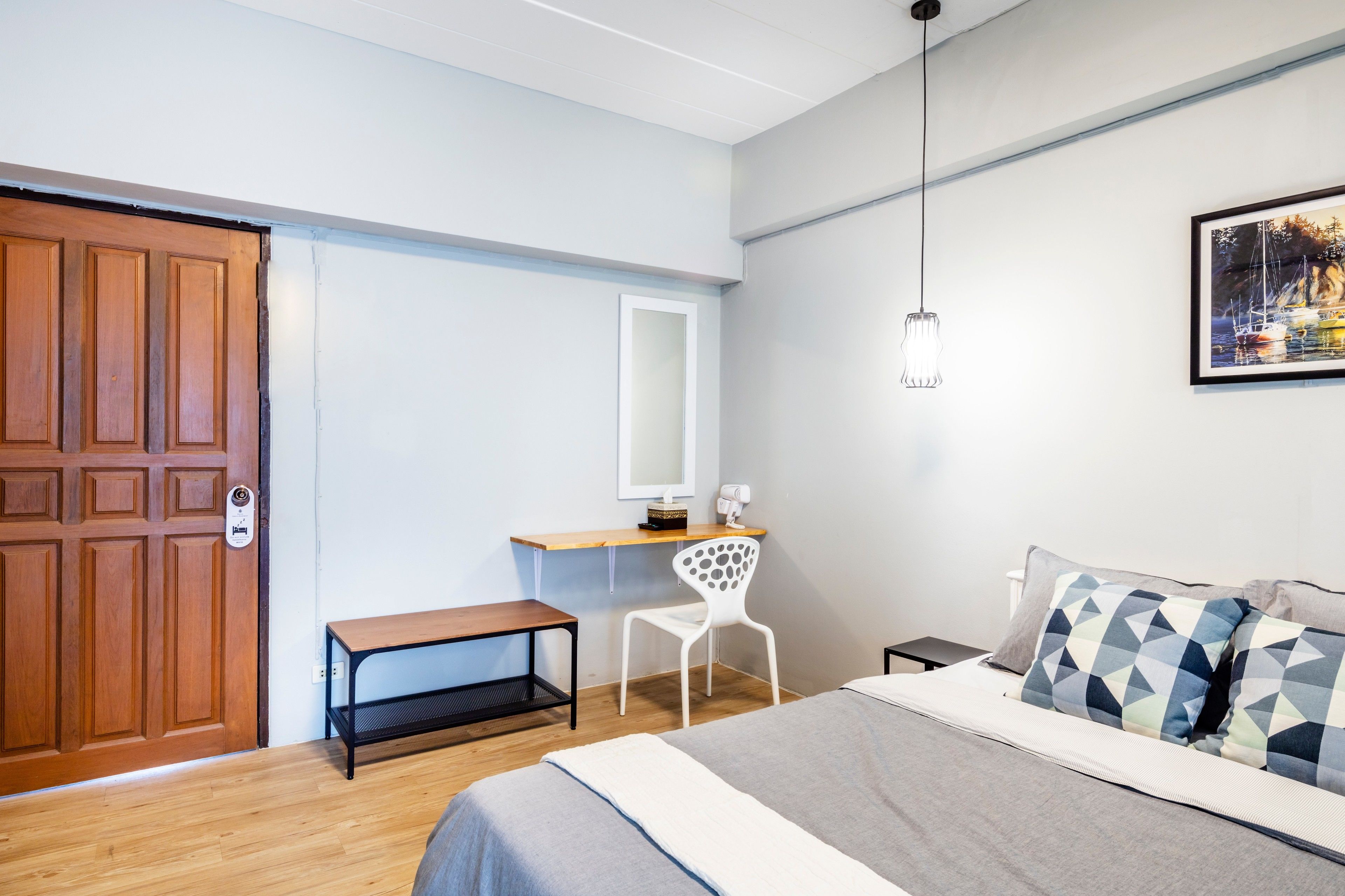 A bedroom with a bed, a desk, a chair, a wooden door, and a painting on the wall.