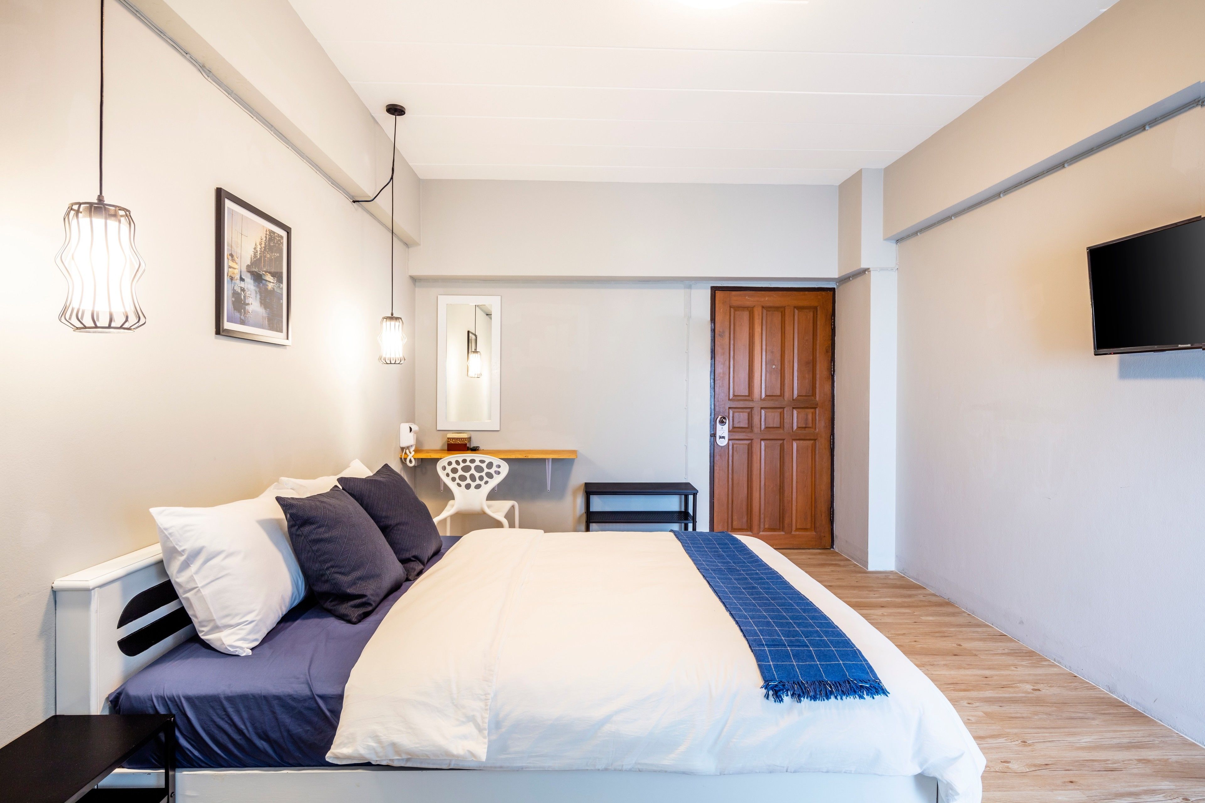 A bedroom with a bed, bedside table, chair, desk, and a TV mounted on the wall.