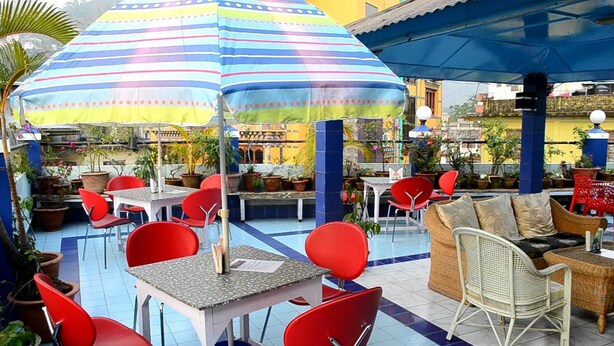 An outdoor seating area with tables and chairs, a striped umbrella, and potted plants. - Hotel Sinchula (Phuntsholing)