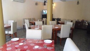 A dining area with tables set for four, chairs, and a television in the background. - Hotel Sinchula (Phuntsholing)