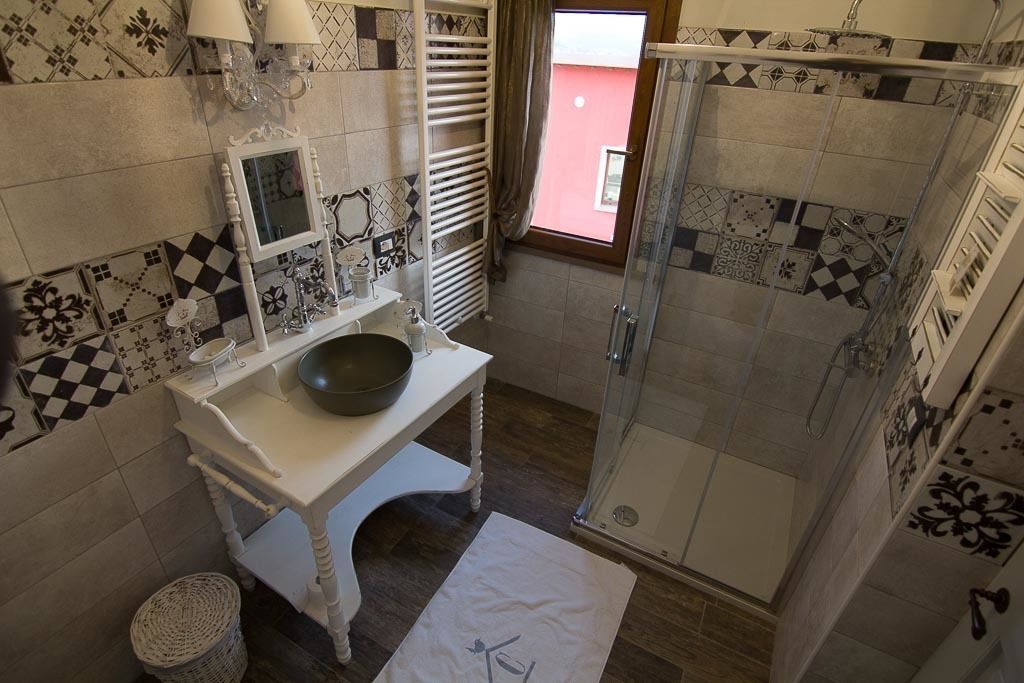 Une salle de bain avec un meuble-lavabo blanc, un grand miroir, un lavabo en forme de cuvette et une douche dotée d’une porte en verre.