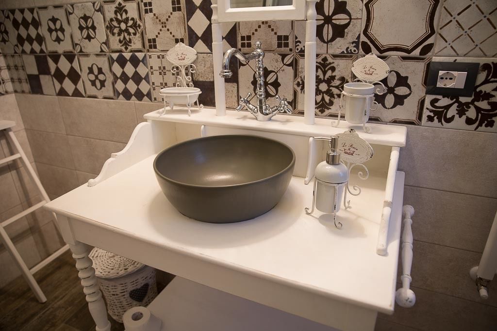 Une salle de bain avec un lavabo blanc, un grand récipient et un miroir décoratif.