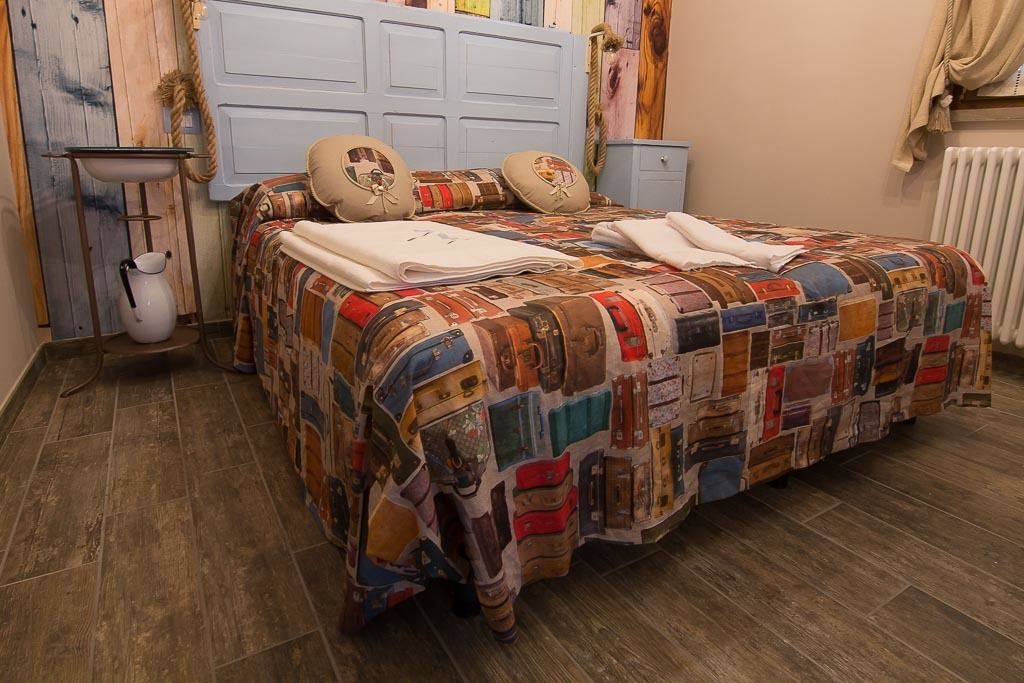 A bed with a patchwork quilt, a bedside table with a pitcher, and a blue headboard.