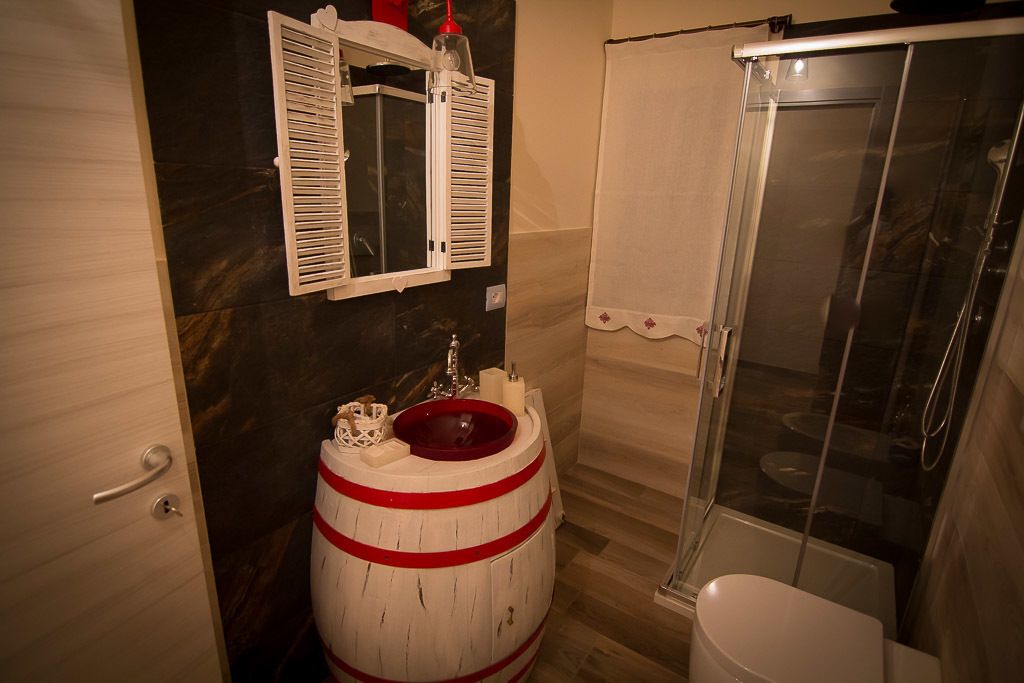 Un baño con un lavamanos de barril de madera, un espejo y un box de ducha.