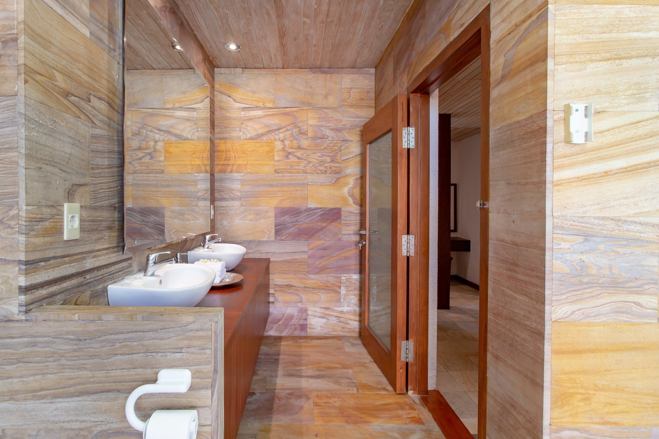 A modern bathroom with marble walls, a wooden vanity, and a glass shower enclosure.