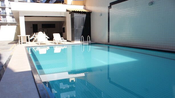 Ein Schwimmbecken mit weißen Liegestühlen und einer gefliesten Wand.