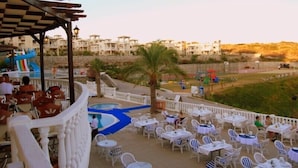 An outdoor terrace with white tables and chairs, a pool, and a view of buildings in the background. - 1 Bedroom Villa Lake View 4 by Likya Global (Milas)