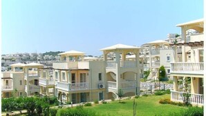 A residential area with multi-story buildings featuring balconies and a view of a hillside. - 1 Bedroom Villa Lake View 4 by Likya Global (Milas)