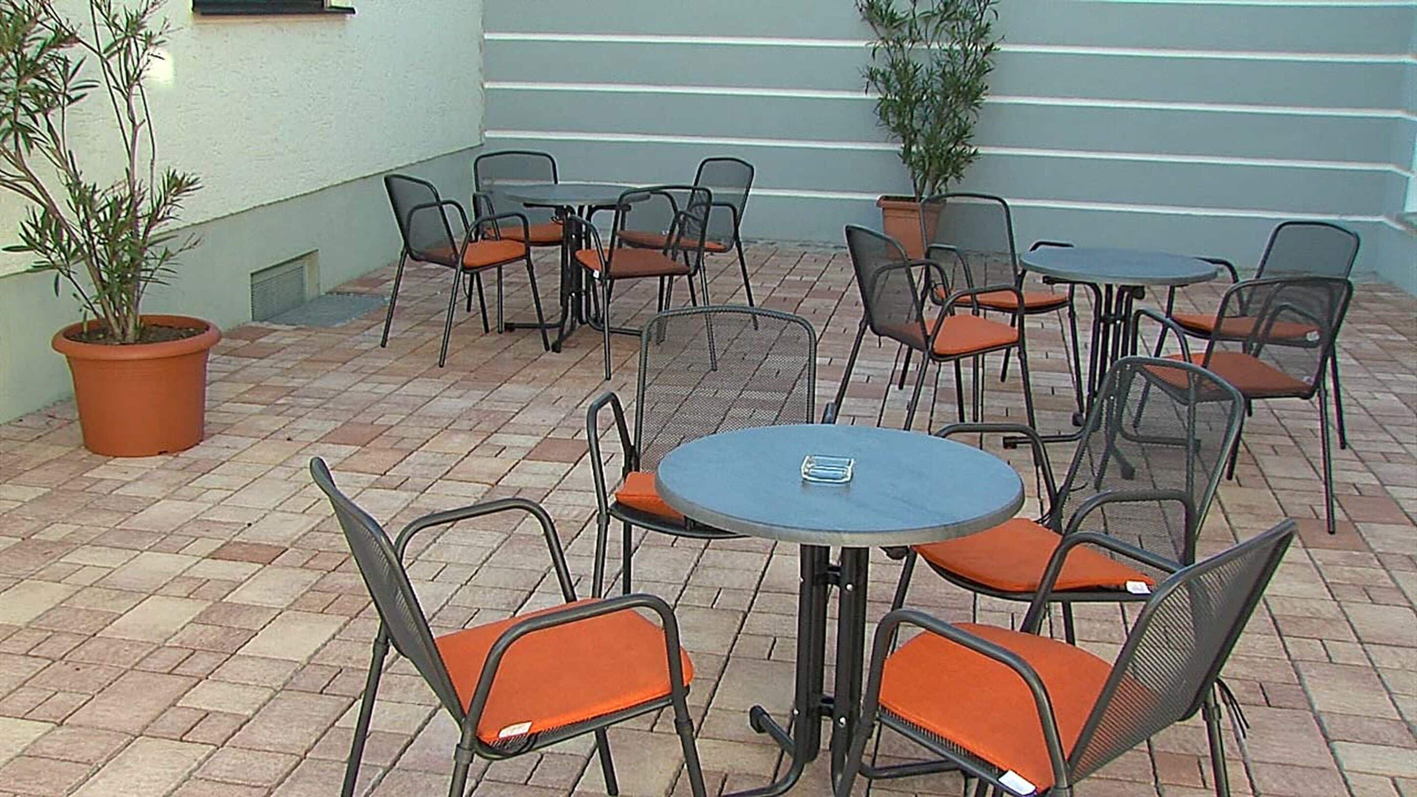An outdoor patio area with round tables and chairs, potted plants, and a tiled floor.