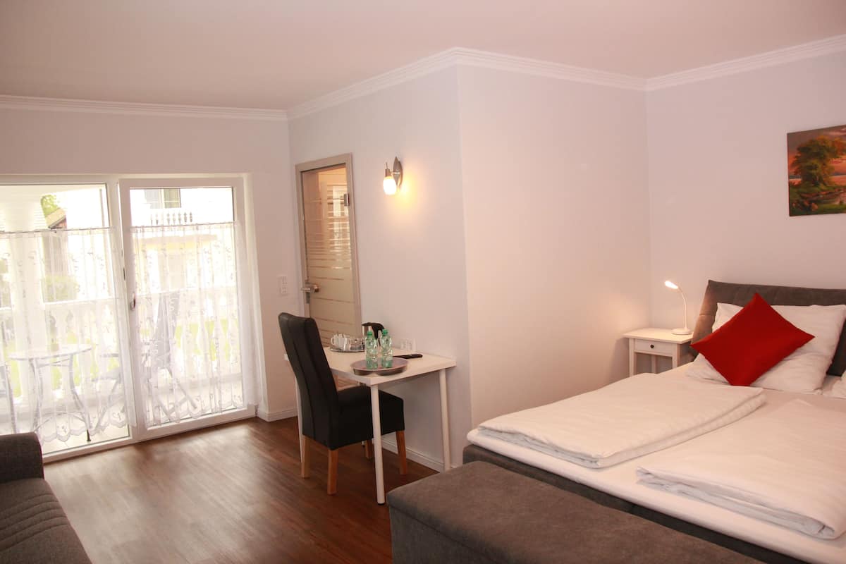 A hotel room with a bed, a desk, a chair, a table, and a balcony with a view.