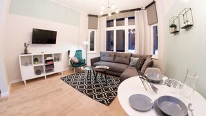 Una sala de estar moderna con un sofá, un televisor, una mesita y una zona de comedor dispuesta con platos y vasos.