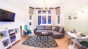 Una sala de estar moderna con un sofá, un televisor, una estantería y un comedor con una mesa y sillas.