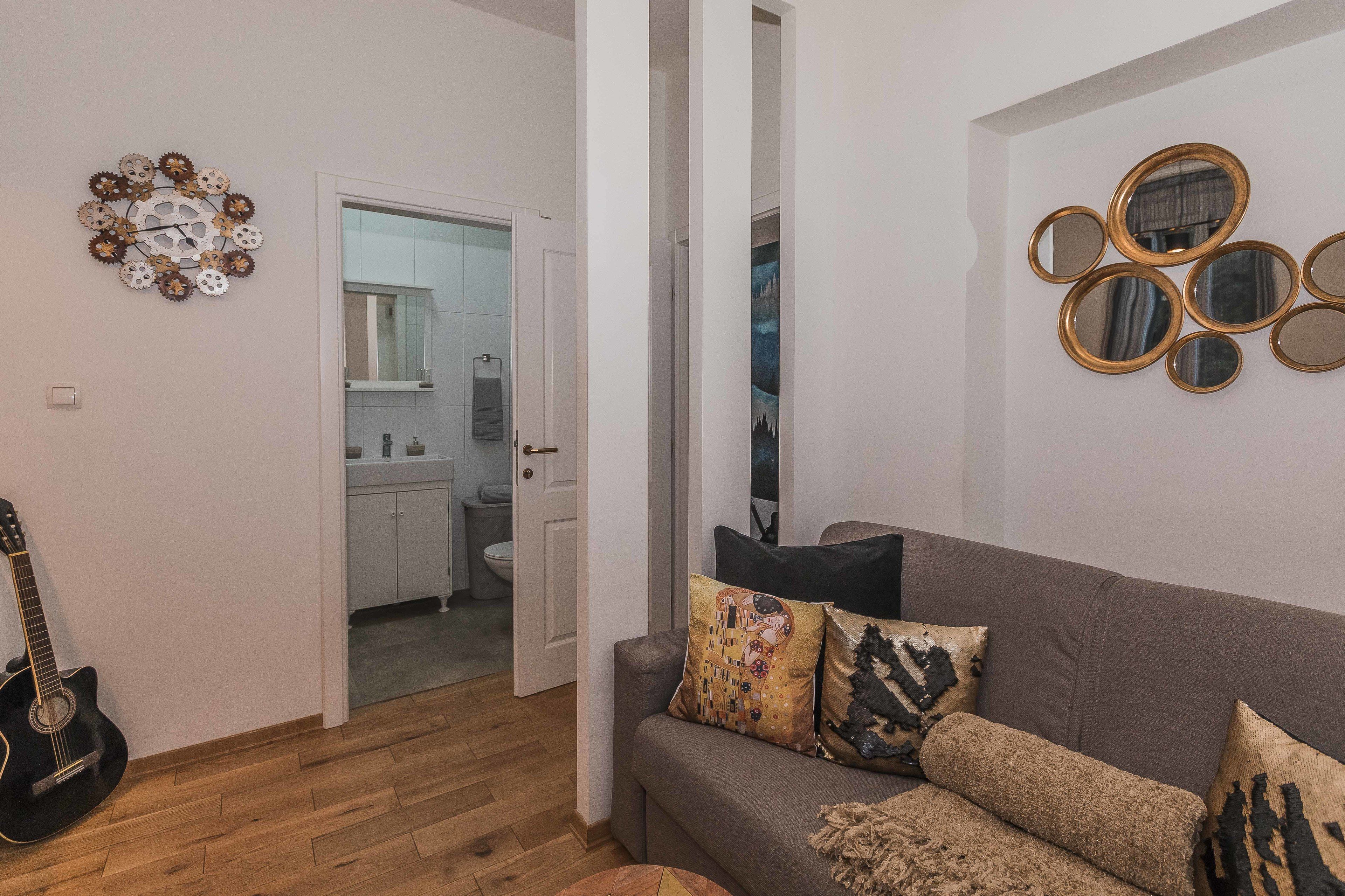 A living room with a grey sofa, a decorative wall clock, and a guitar.
