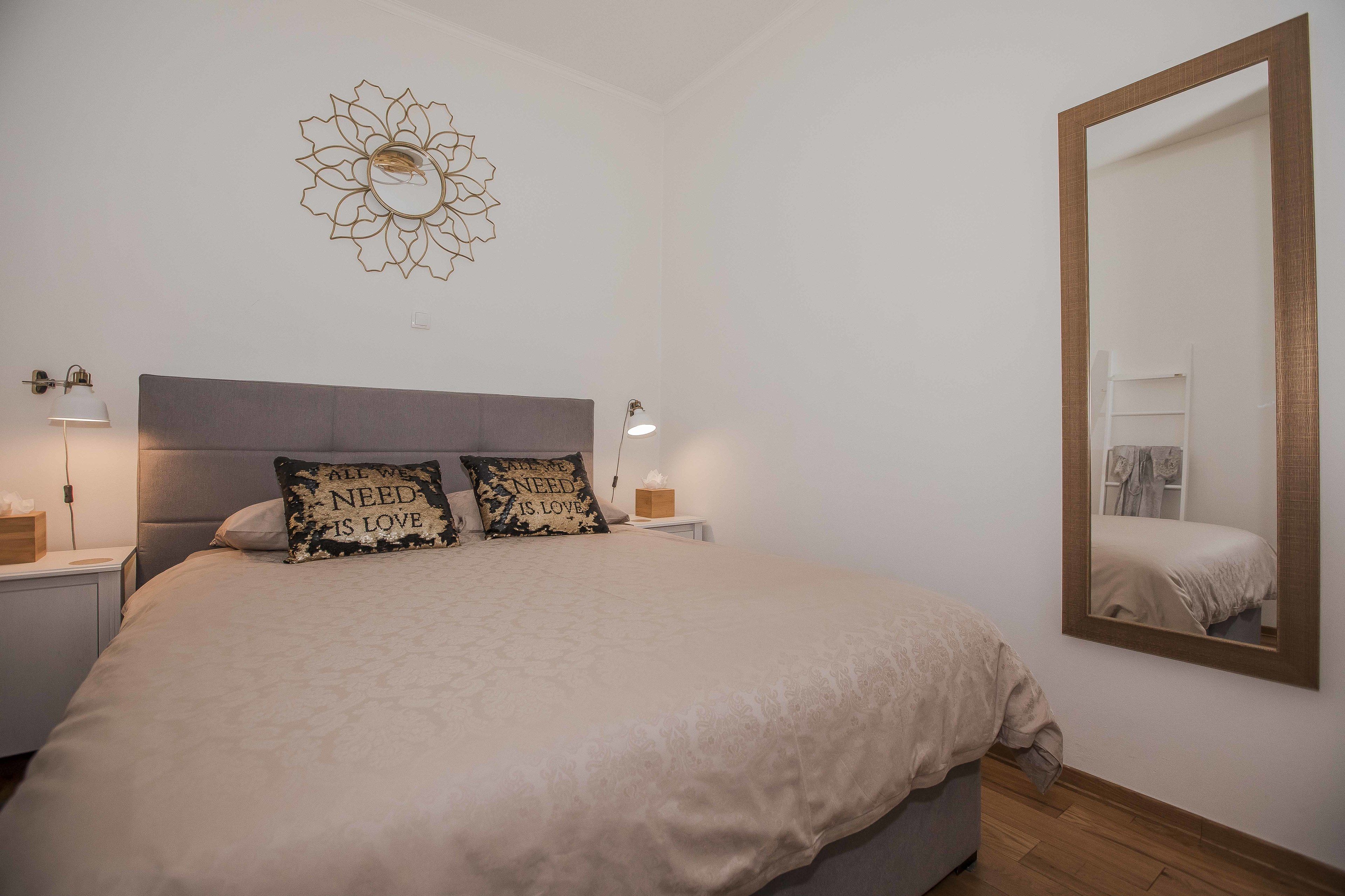 A bedroom with a large bed, two bedside lamps, a wall mirror, and a decorative wall piece.