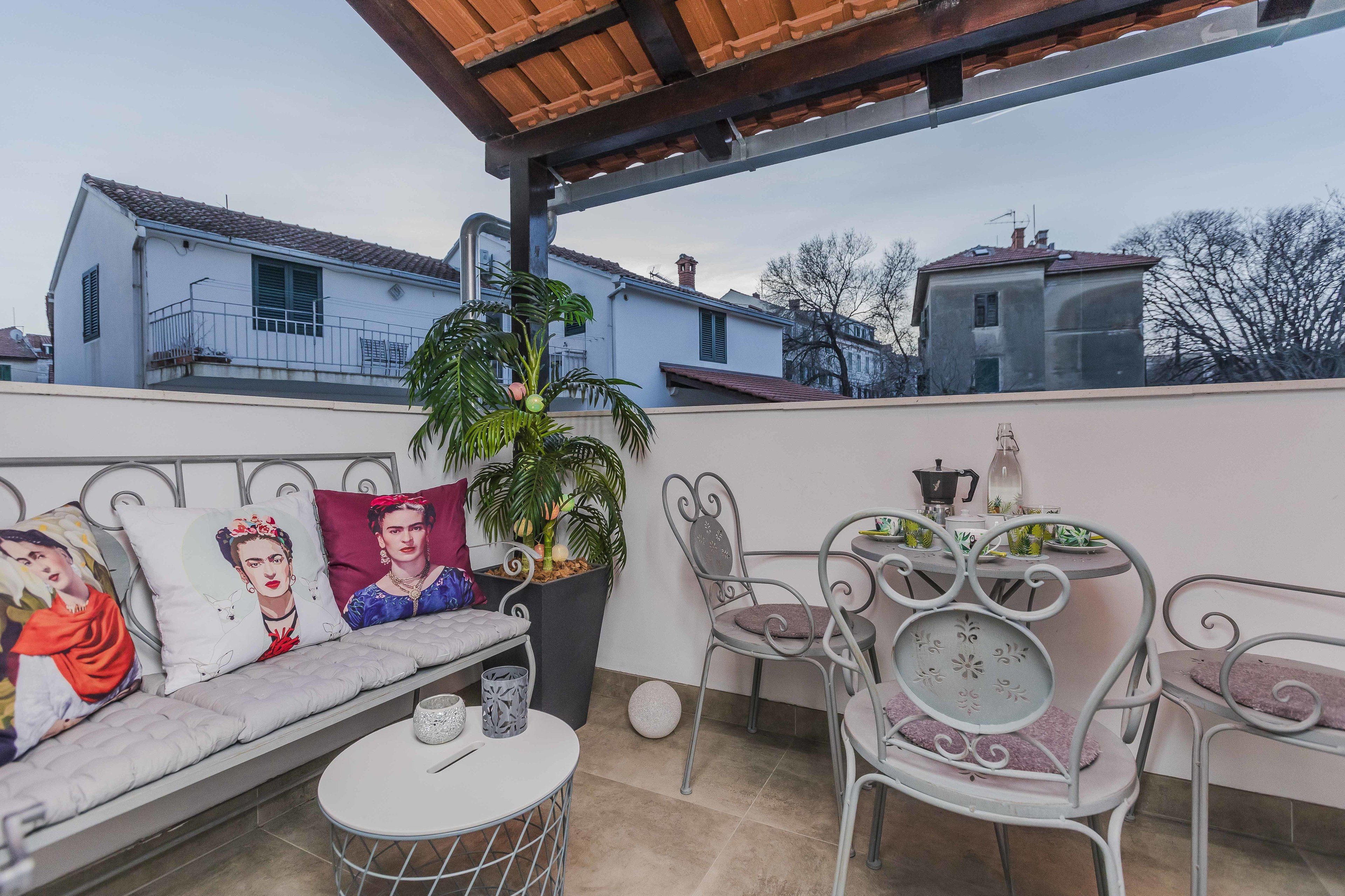 A balcony with a sofa, chairs, a table, and a potted plant.