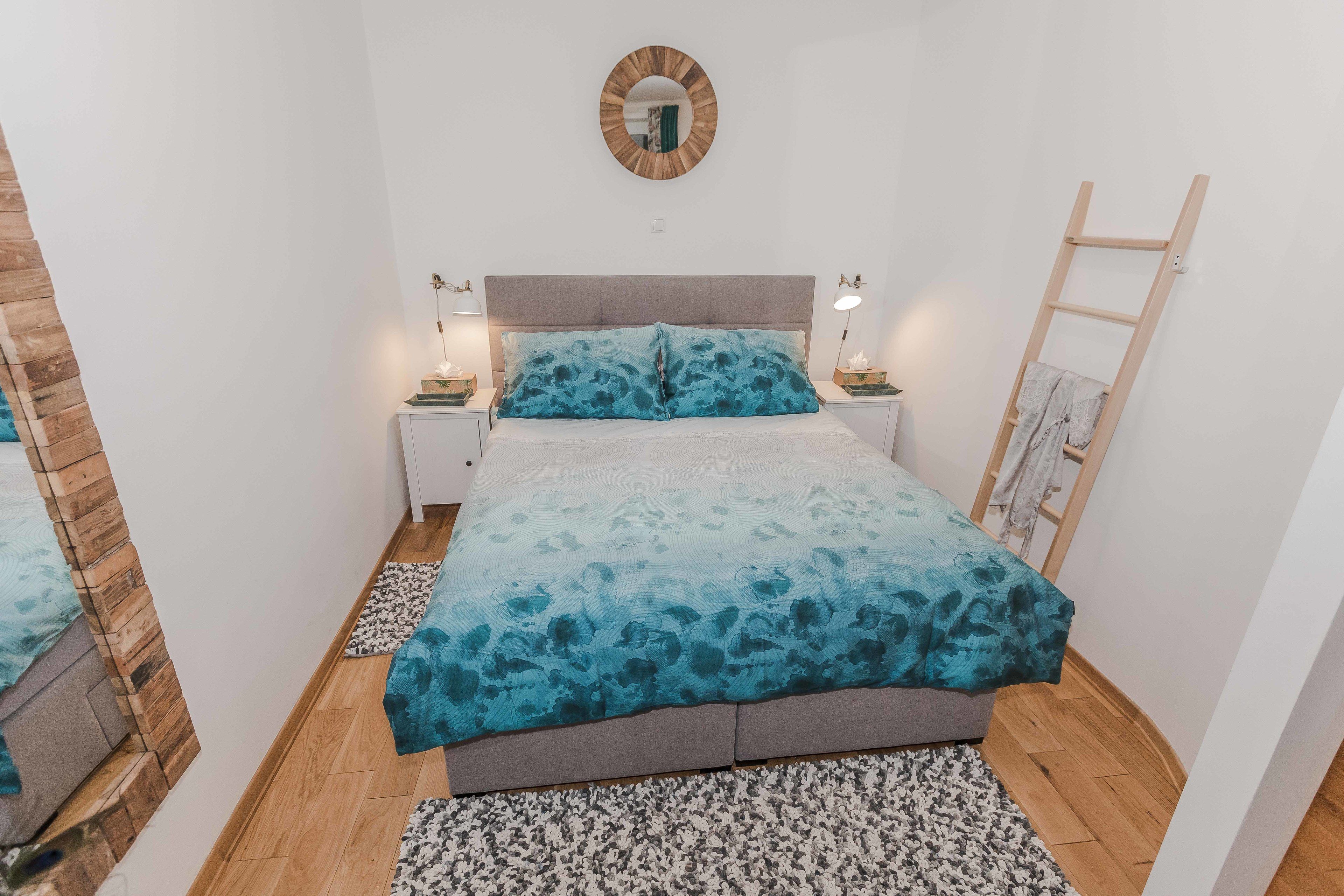 A bedroom with a bed, nightstands, a mirror, and a wooden ladder.