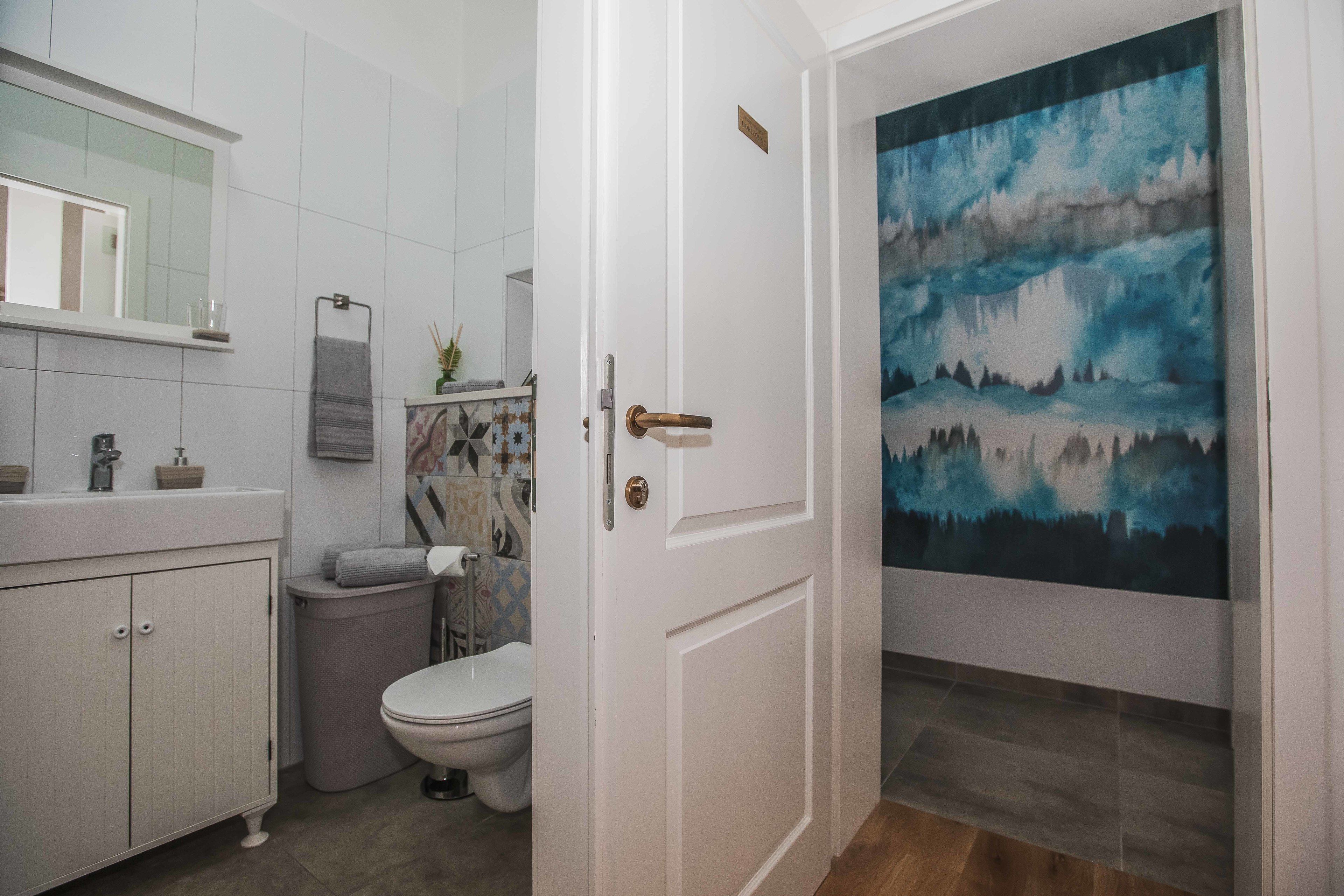 Un baño con inodoro, lavamanos y armario, un cuadro en la pared y una puerta con pomo de latón.