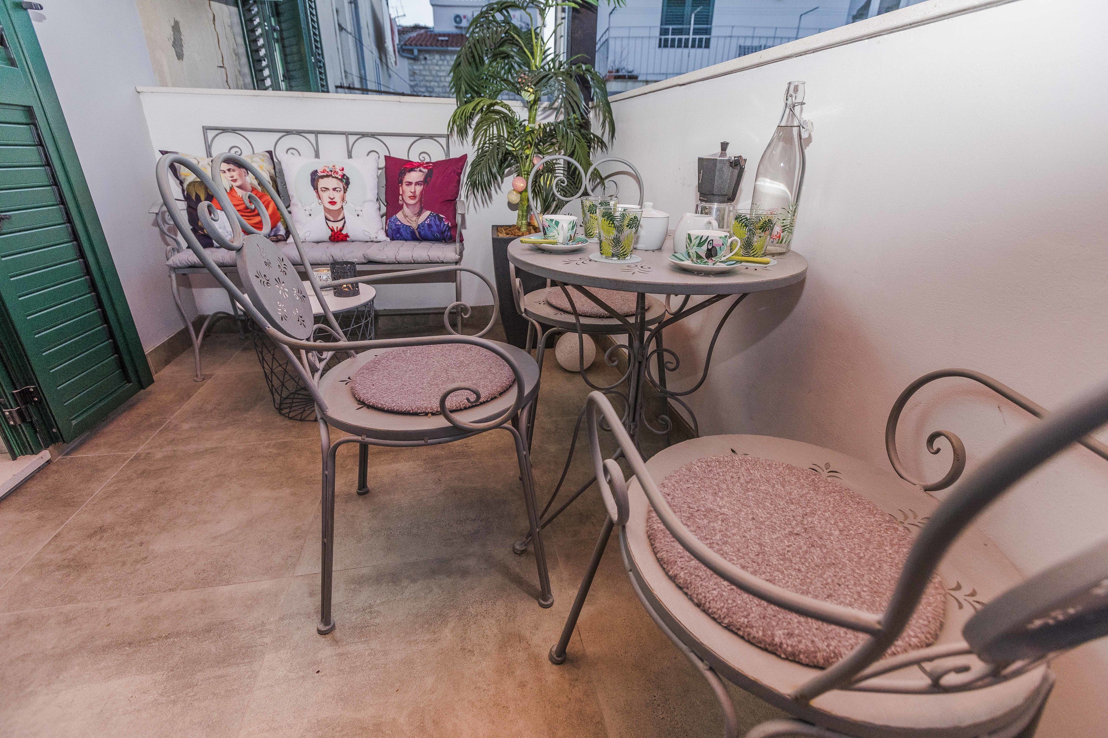 A balcony with a metal table and chairs, a potted plant, and a bottle.