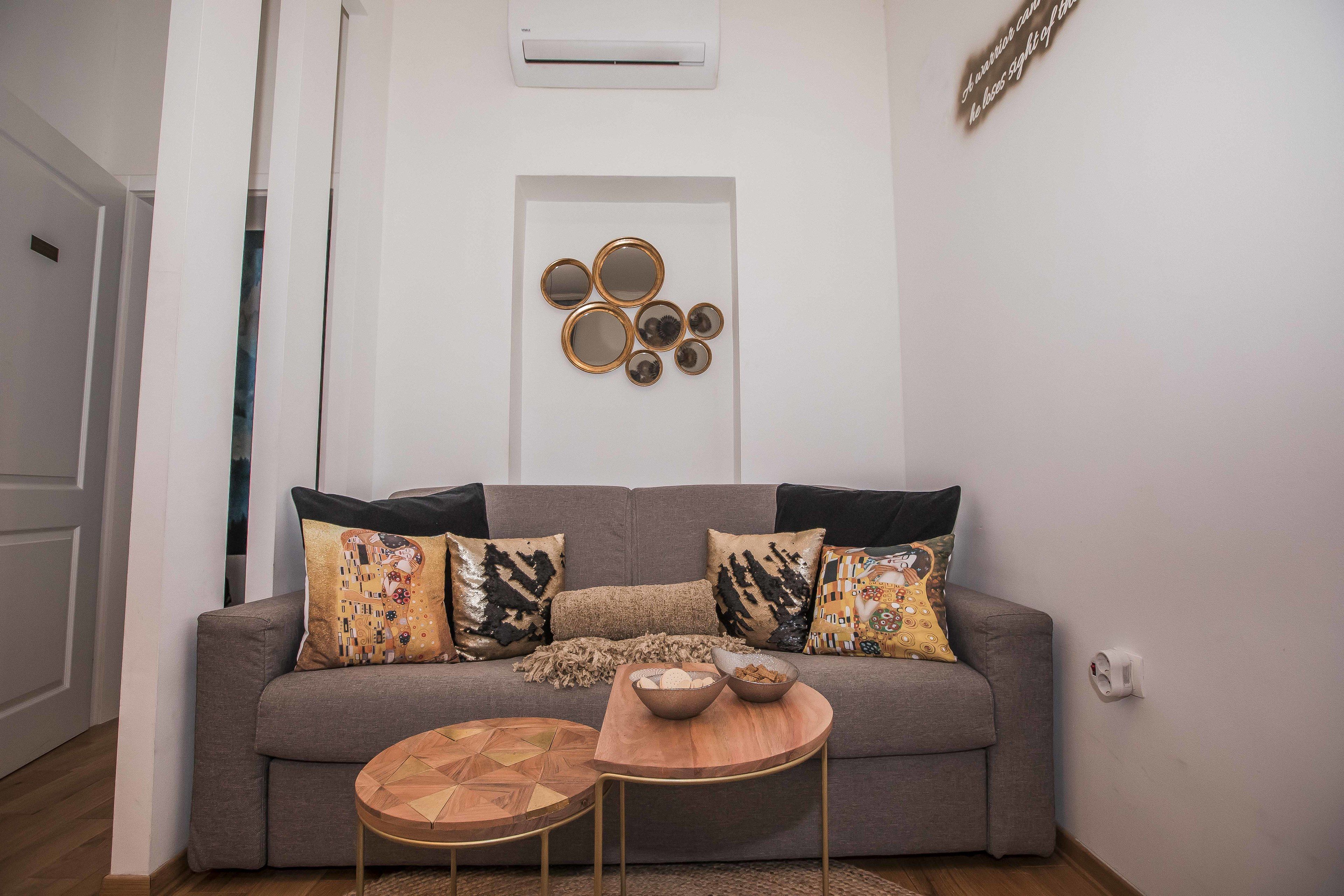 Una sala de estar con un sofá gris, cojines estampados, una mesa de centro de madera y un espejo decorativo colgado en la pared.