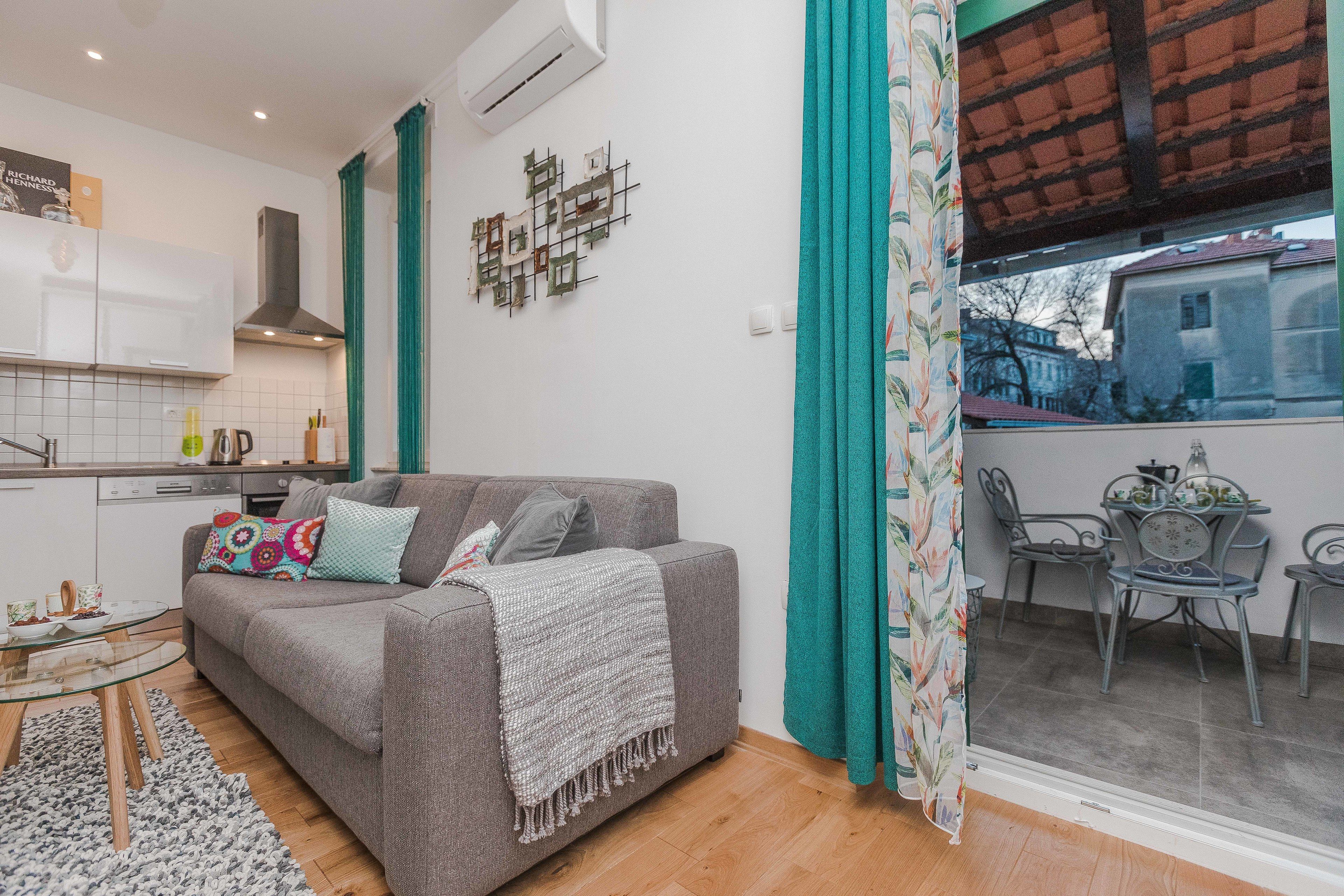 A living room with a grey sofa, a glass coffee table, and teal curtains.