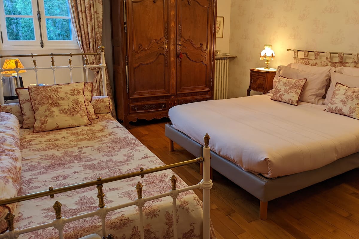 Ein Schlafzimmer mit einem großen Bett, einem kleineren Bett, einem Kleiderschrank und einem Nachttisch mit einer Lampe.