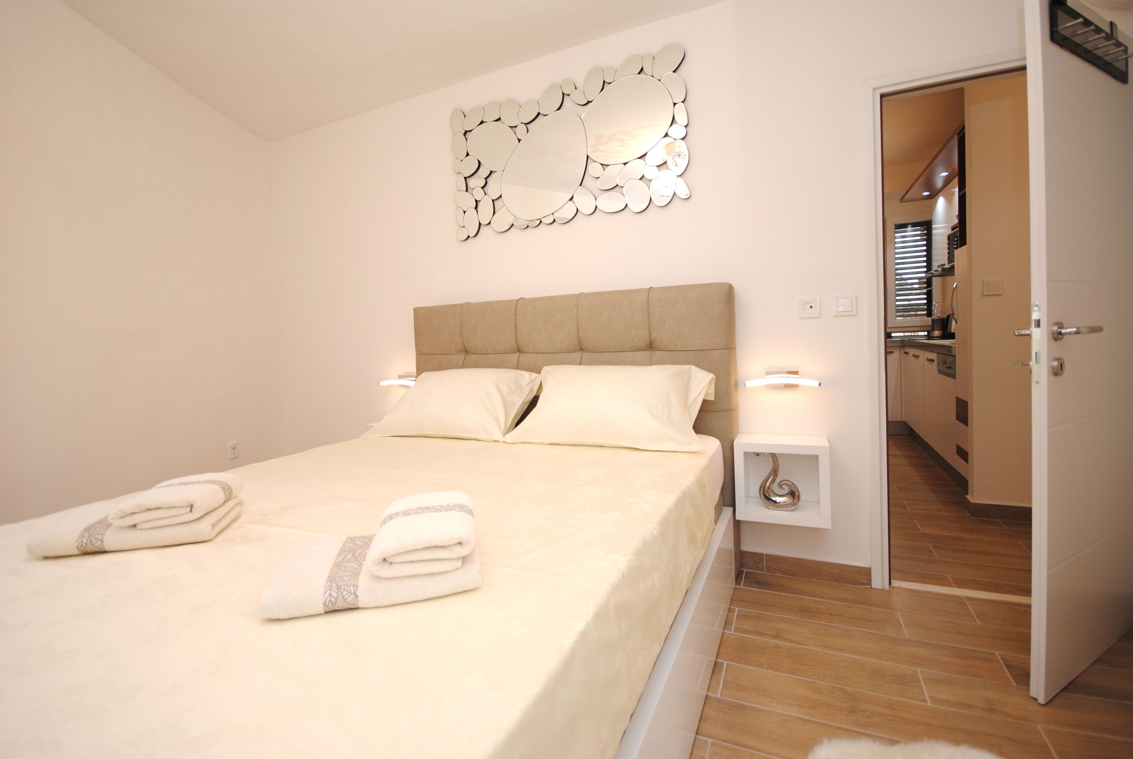 A neatly made bed with pillows and folded towels, a bedside table with a lamp, and a decorative wall piece.