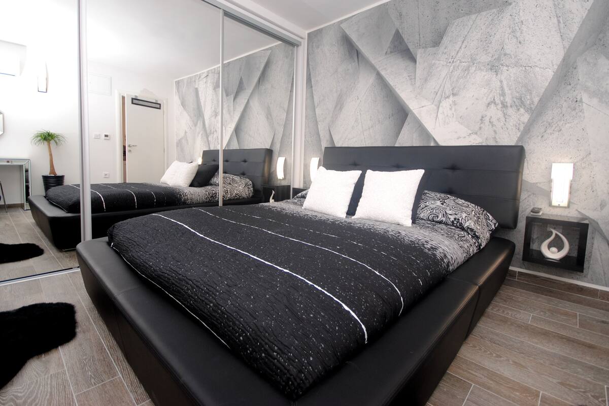 Un dormitorio moderno con una cama grande, un espejo y un diseño geométrico en la pared.