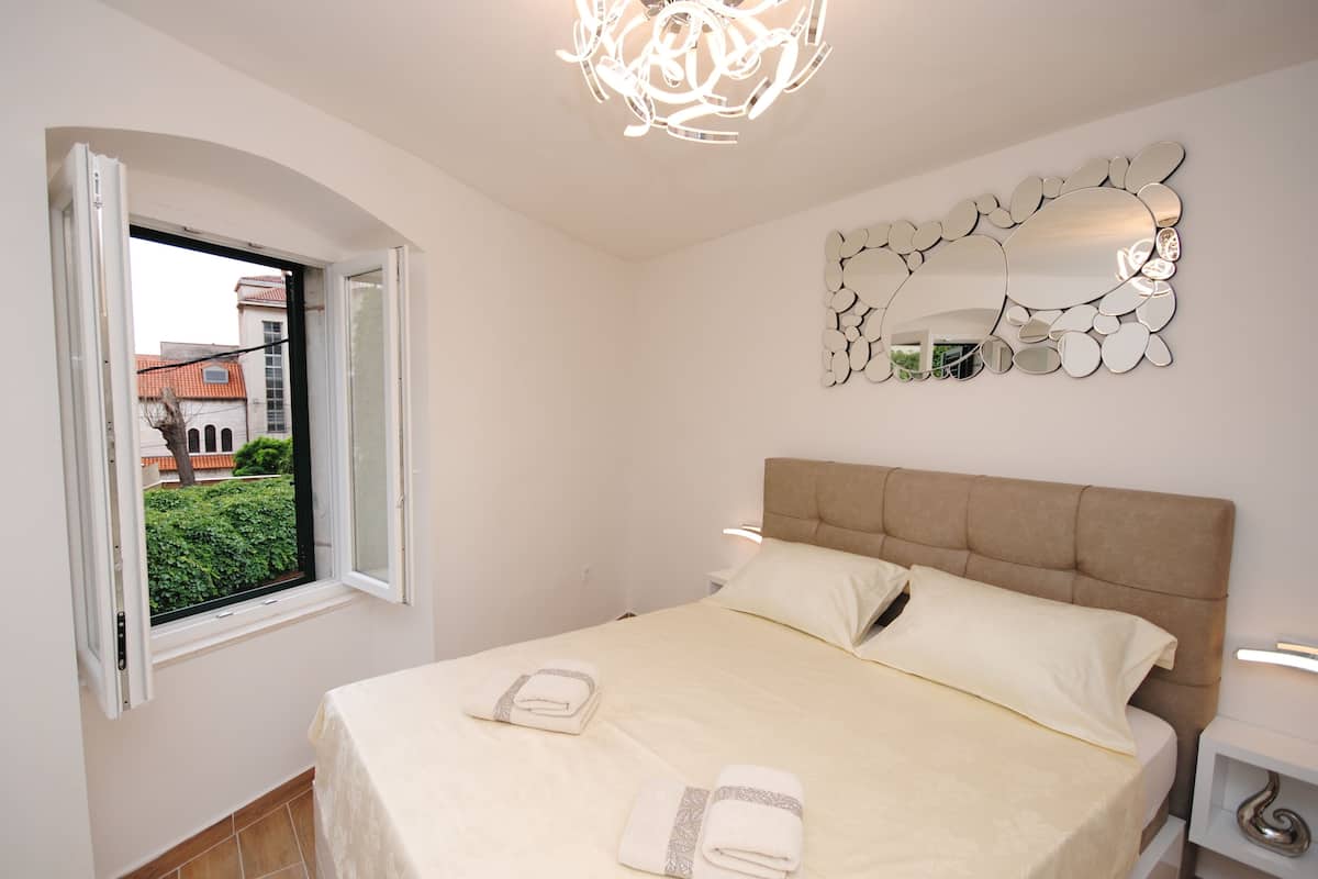 Una cama bien hecha con toallas, una ventana con vistas despejadas, una lámpara moderna y un espejo decorativo en la pared.