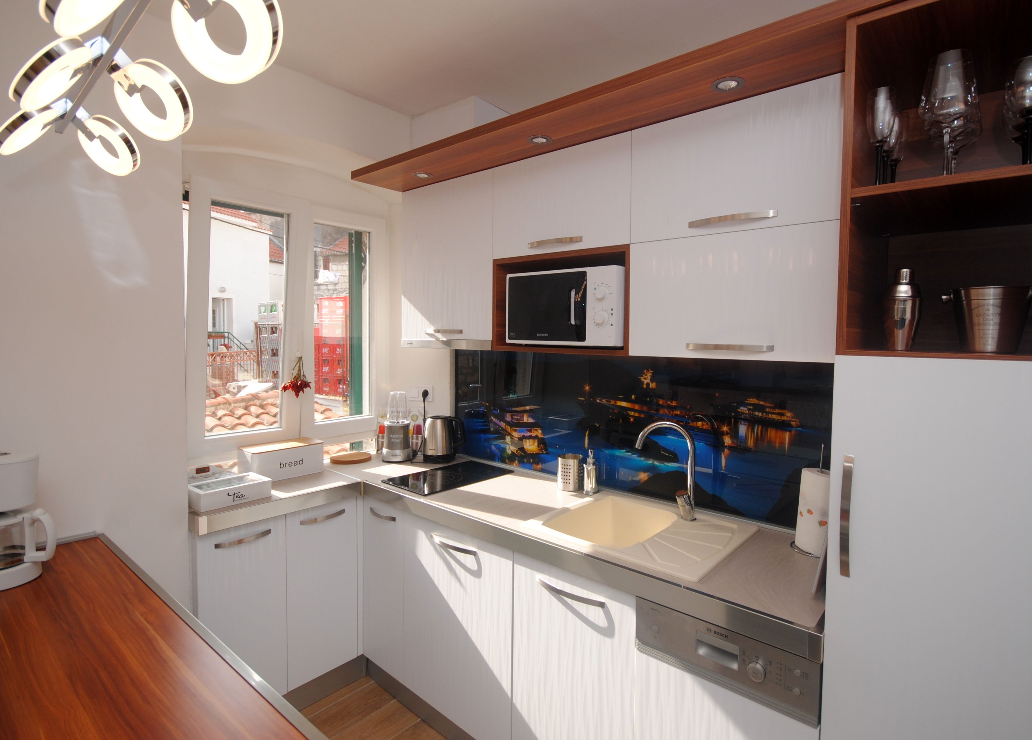 A modern kitchen with white cabinets, a built-in microwave, a sink, and a coffee machine.