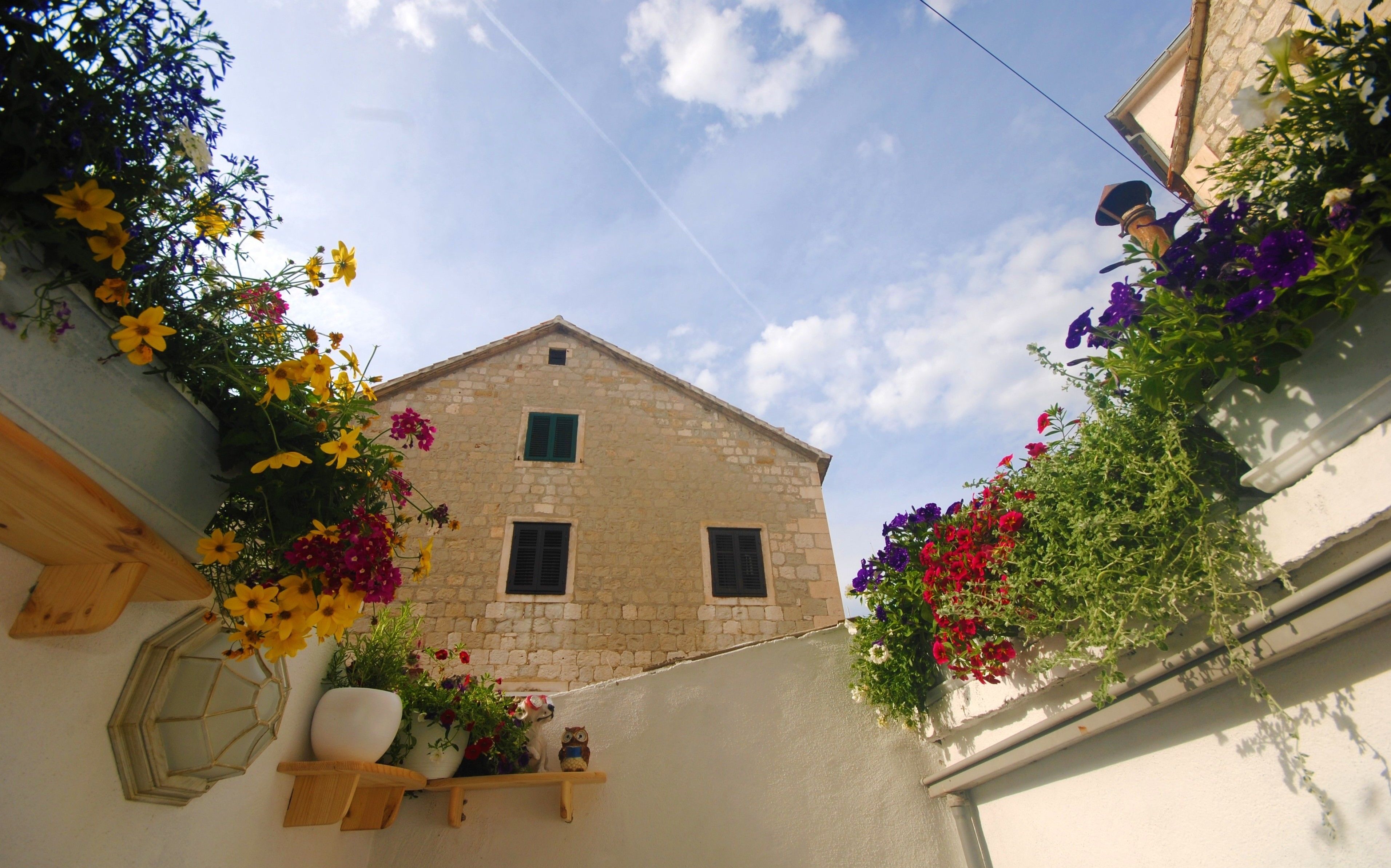A stone building with a sloped roof, a small window with shutters, and a flower box with various flowers.