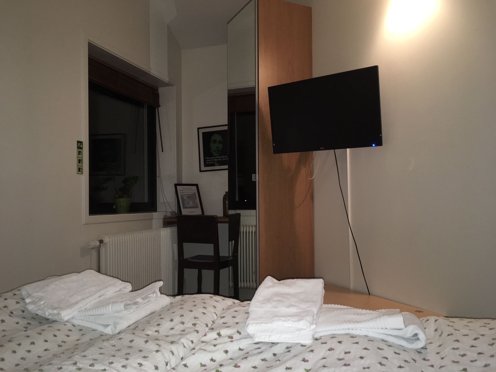 A hotel room with a bed, a chair, a desk, a television mounted on the wall, and a window.