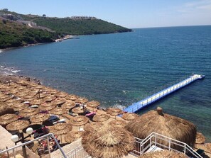 A beach with thatched umbrellas and a pier extending into the sea. - 1 Bedroom Apartment Lake View 9 by Likya Global (Milas)