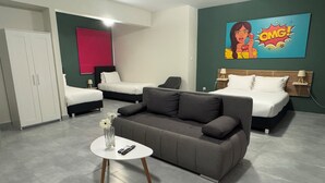 A modern hotel room with two single beds, a grey sofa, a small round table with a vase and remote control, and a vibrant comic book artwork on the wall. - Connect Suites (Athens)