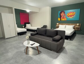 A modern hotel room with two single beds, a grey sofa, a small round table with a vase and remote control, and a vibrant comic book artwork on the wall. - Connect Suites (Athens)