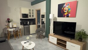 A modern living room with a flat-screen TV, a dining area with chairs, a kitchen with cabinets, and a painting on the wall. - Connect Suites (Athens)