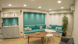 A modern living room with teal sofas, a wooden coffee table, and a white side table. - Connect Suites (Athens)