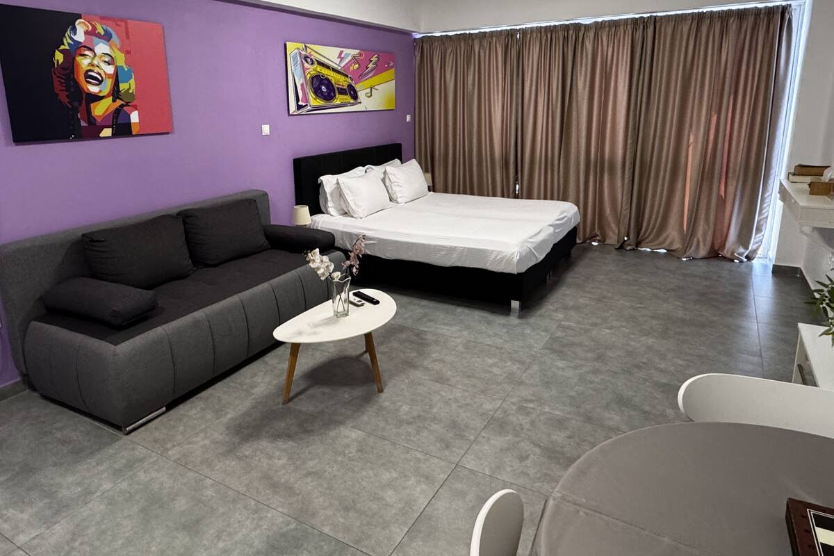 Una habitació d'hotel moderna amb un llit, un sofà, una taula petita amb un ram i dos quadres a la paret.