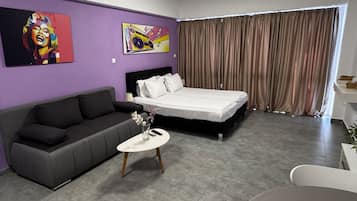 Una habitación de hotel moderna con cama, sofá, una mesita con un florero y dos cuadros en la pared.
