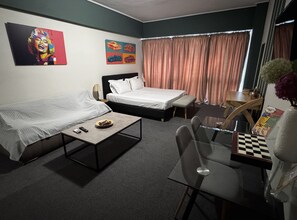 A hotel room with a bed, a sofa, a small table, a chair, a desk, a vase with flowers, and two paintings on the wall. - Connect Suites (Athens)