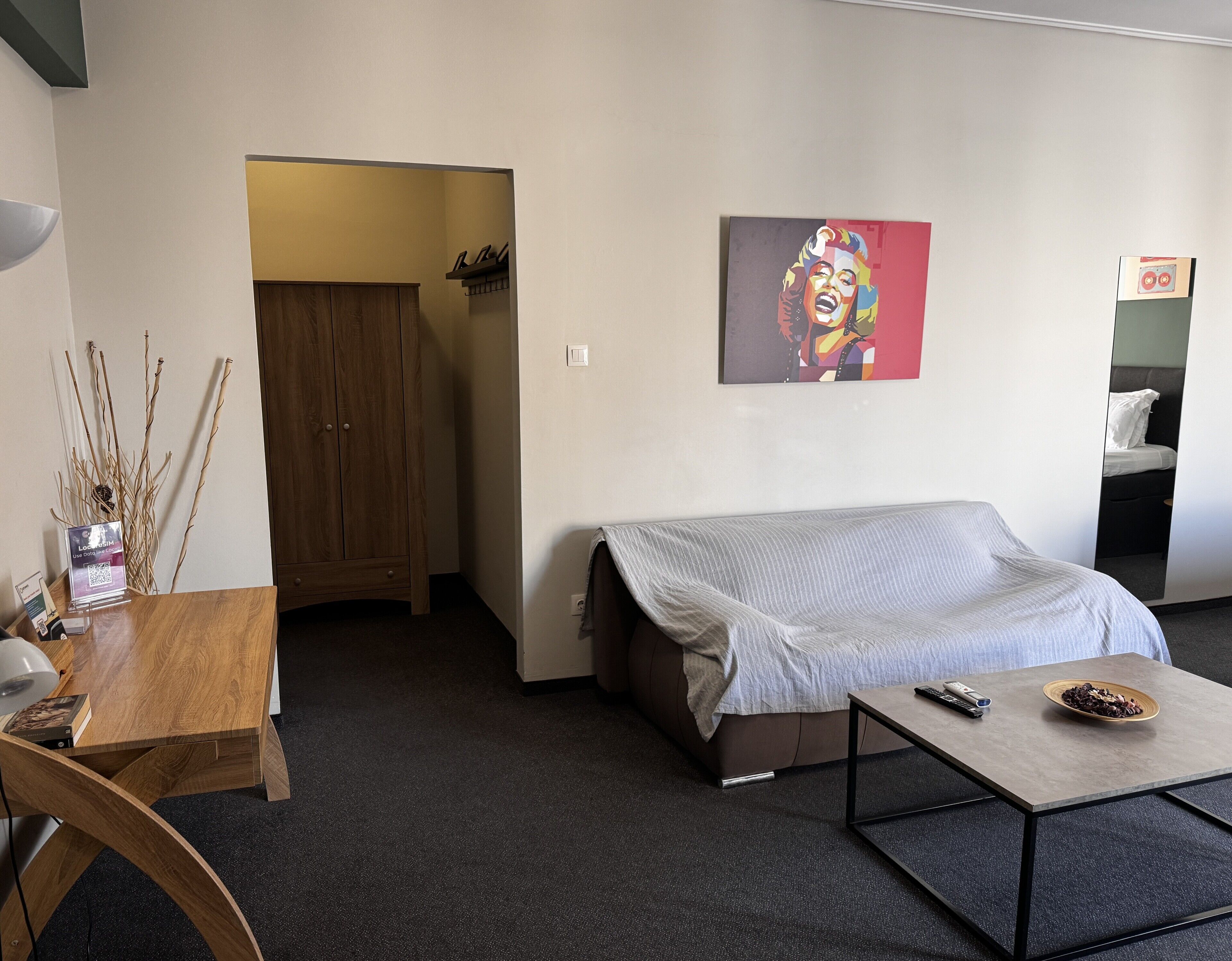 A room with a bed, a desk, a chair, a coffee table, and a painting on the wall.