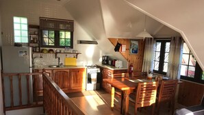 Eine geräumige Küche mit Holzsäulen, ein Essbereich mit Holztisch und -stühlen sowie eine Treppe, die in eine obere Etage führt.