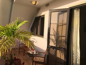 Un balcón con una mesa y sillas, una planta en maceta y una puerta corrediza de vidrio.