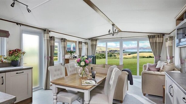 A spacious room with a dining table, chairs, a sofa, and a kitchen area. - Newperran Holiday Resort (Truro)