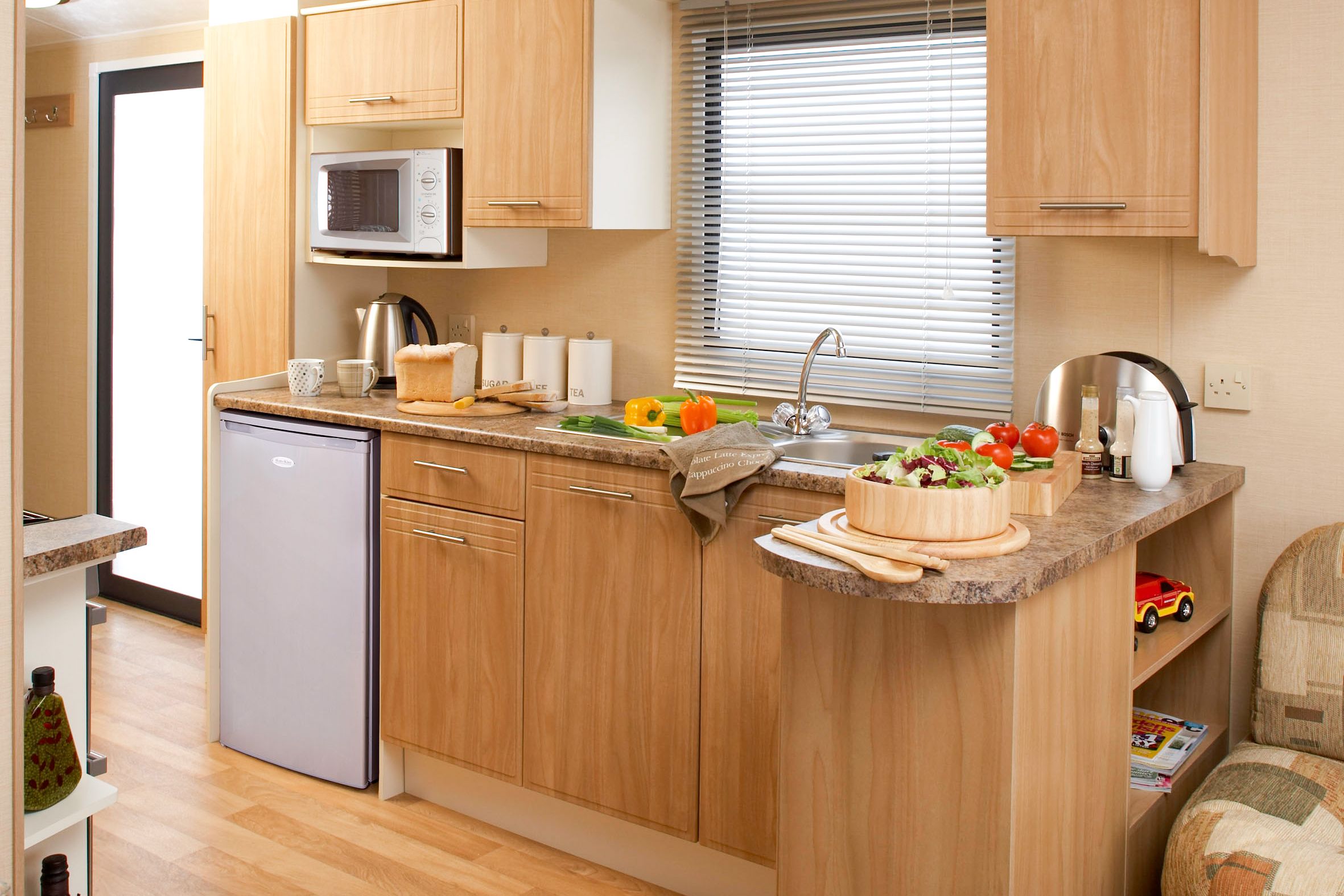 A compact kitchen with wooden cabinets, a built-in microwave, a sink, and a small refrigerator.