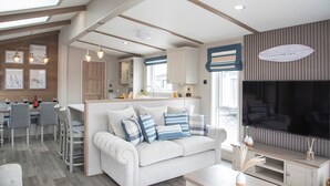 A modern living room with a sofa, TV, and dining area. - Newperran Holiday Resort (Truro)