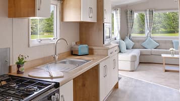 A modern kitchen with a gas stove, sink, and wooden cabinets. There is a dining area with a sofa and a small table.