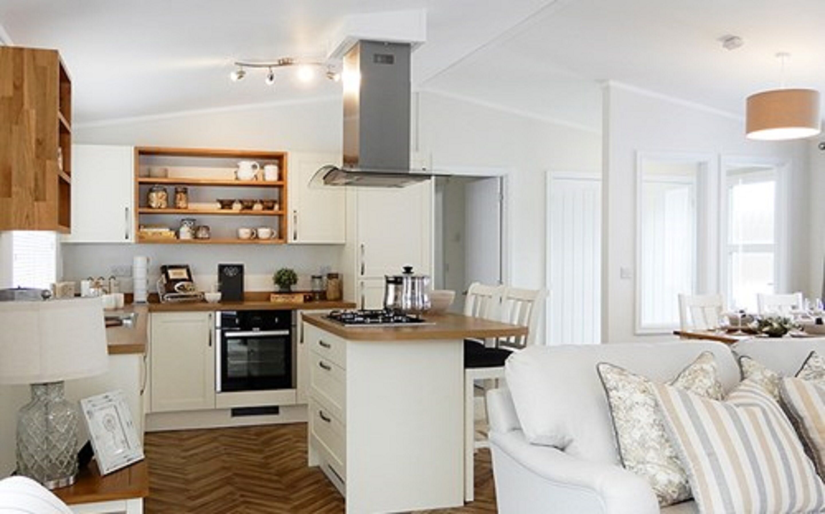 A modern kitchen with white cabinets, a central island, and a dining area with a white sofa.